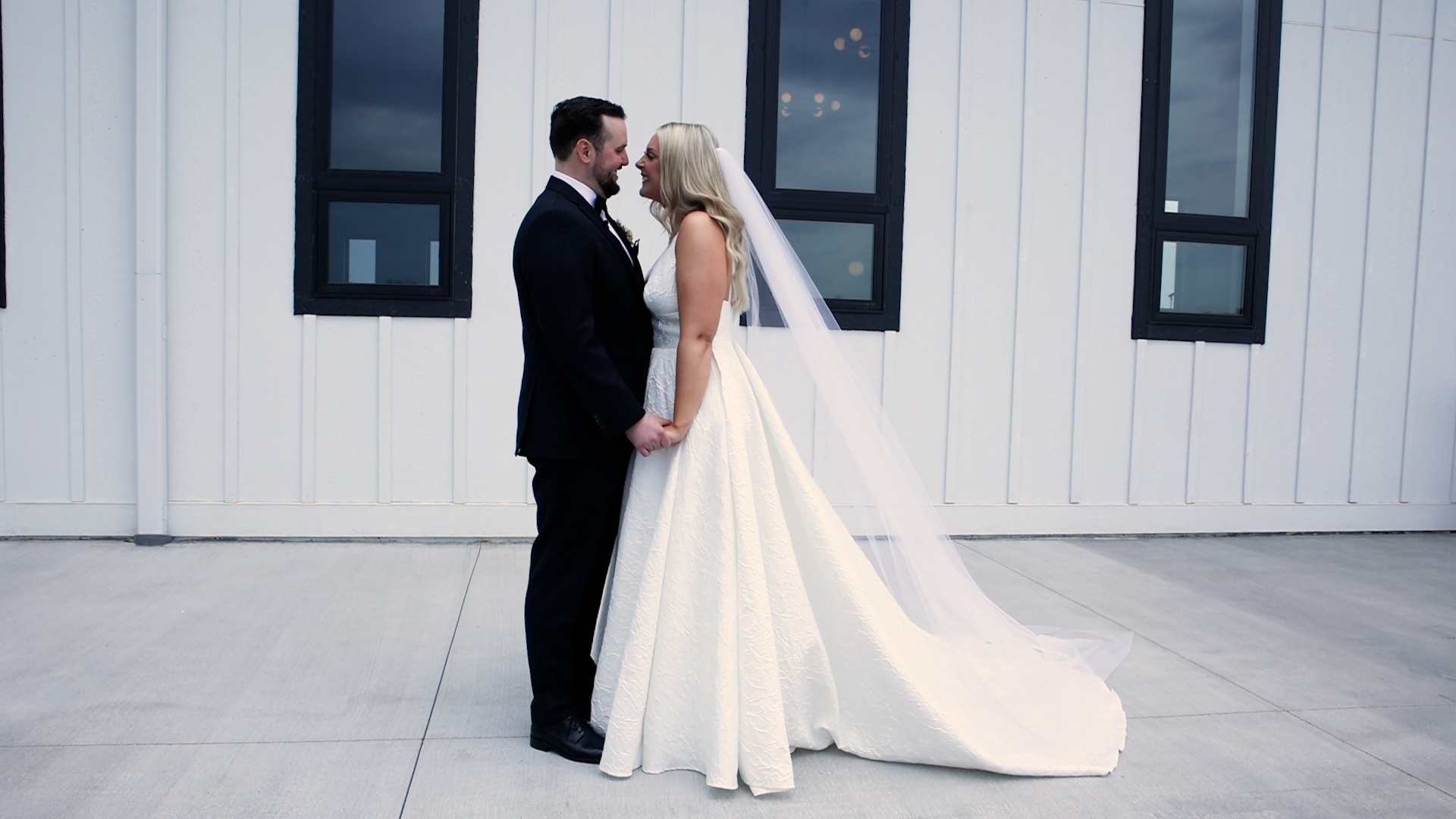 Newlyweds stand belly button to belly button in front of a white wall with black framed windows Woodhaven weddings